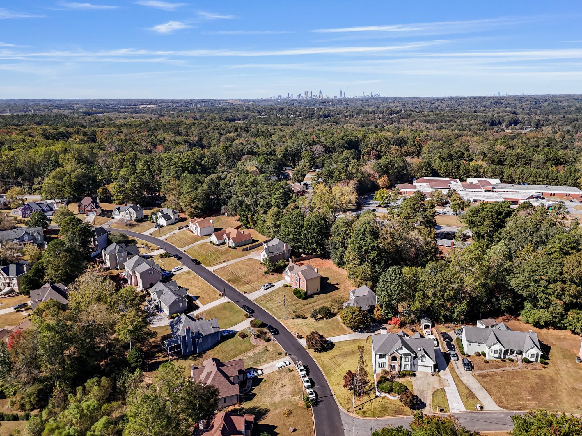 Aerial view of a wooded suburban Atlanta neighborhood with single-family homes and the downtown Atlanta skyline visible in the distance