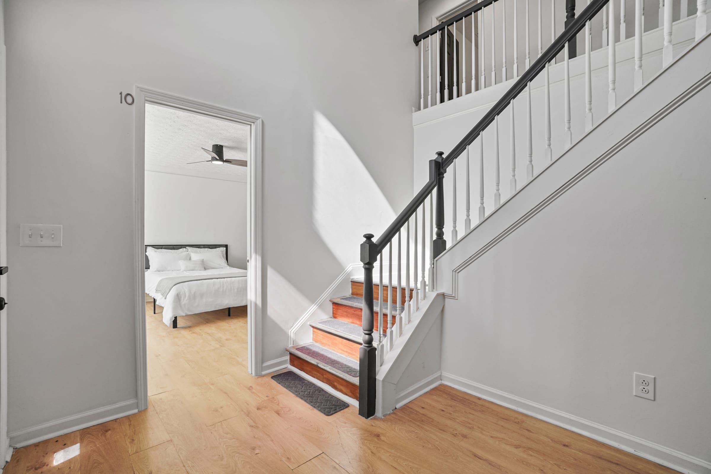 Bright entryway and staircase with wood flooring inside a renovated co-living home, with a numbered bedroom door visible in the background