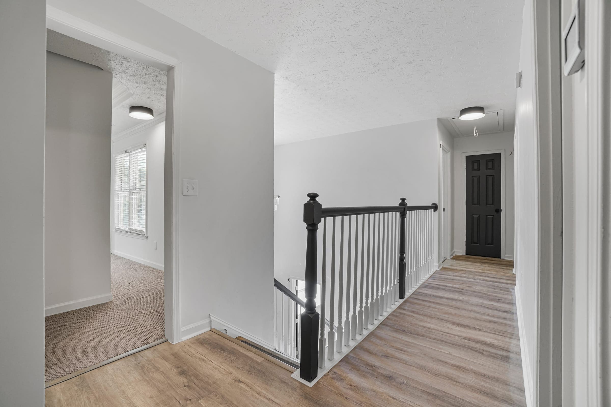 Upstairs hallway with numbered bedroom doors, black stair railing, and wood-look flooring in a professionally managed co-living property