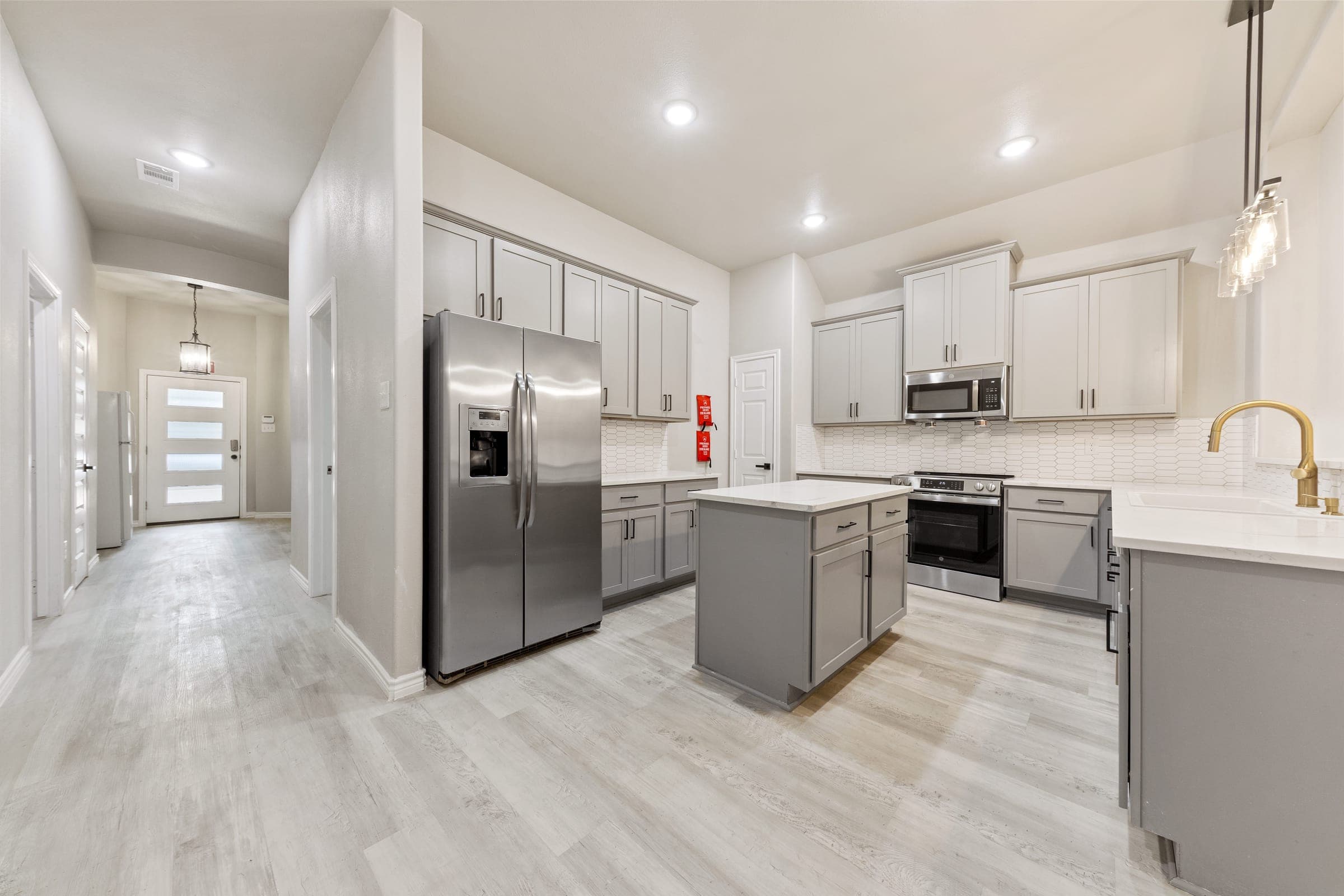 Renovated kitchen with gray shaker cabinets, stainless steel appliances, quartz countertops, and a gold faucet