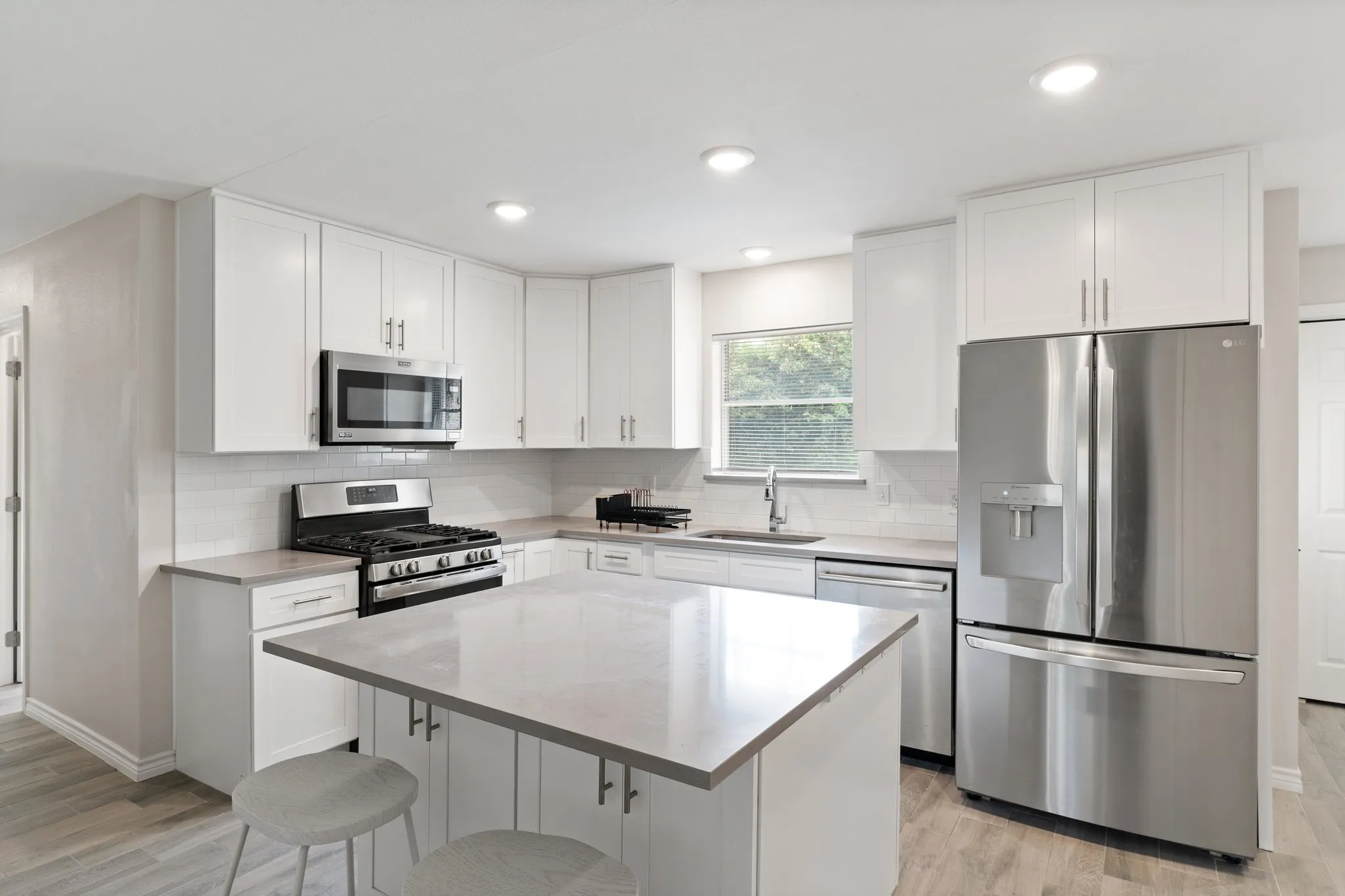 Renovated kitchen with white shaker cabinets, a center island, stainless steel appliances, and quartz countertops
