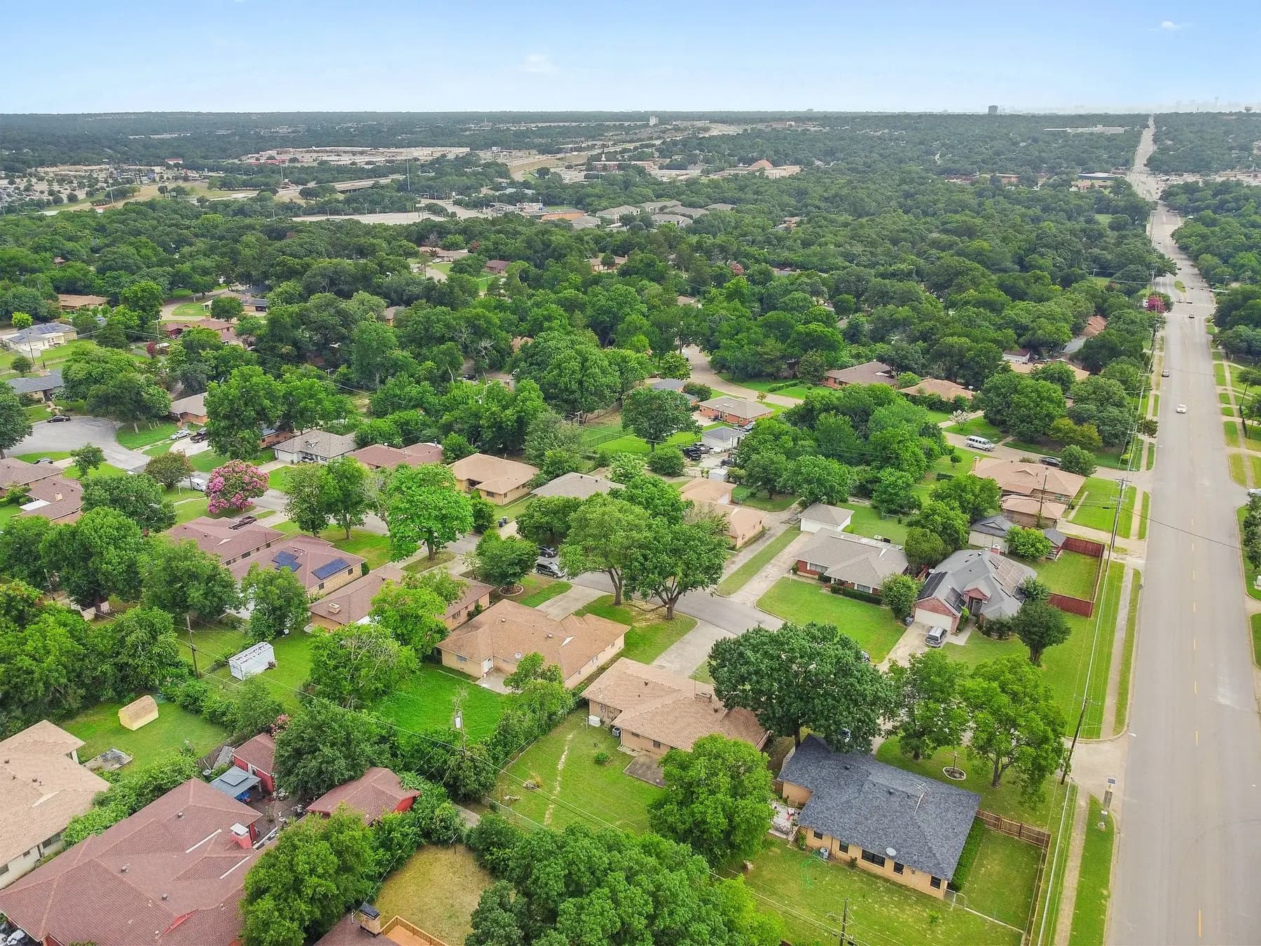 Aerial view of a tree-lined residential neighborhood in Dallas, Texas with single-family homes along a main road
