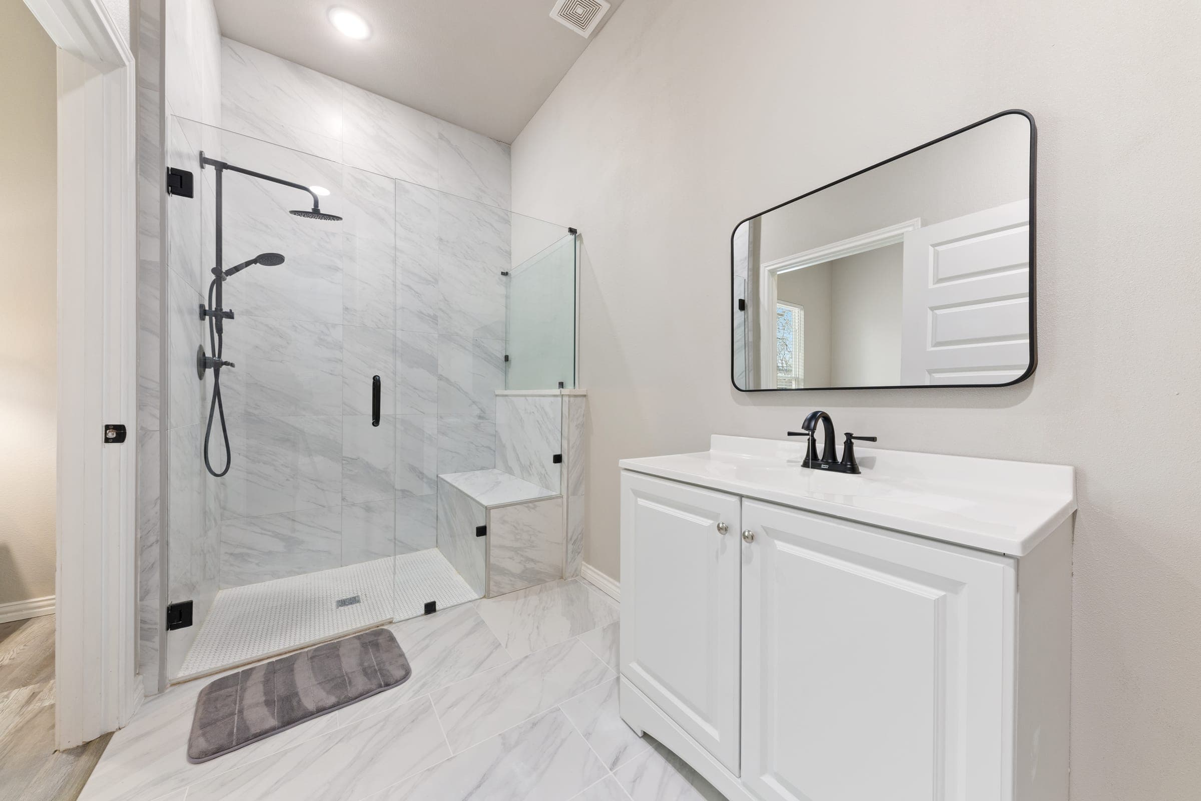 Renovated bathroom with a marble-tiled walk-in glass shower, built-in bench, and a white vanity with matte black fixtures
